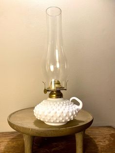 a white vase sitting on top of a wooden table next to a light bulb lamp