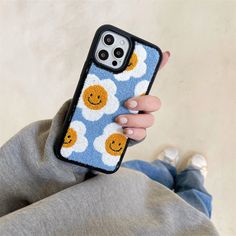 a person holding up a phone case with smiley faces on it and clouds in the background