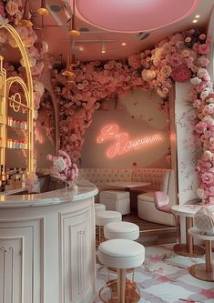 the interior of a fancy restaurant decorated with pink flowers and gold accents, along with white stools