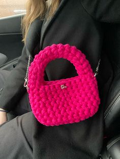 a pink crocheted purse sitting on the back seat of a car in someone's lap