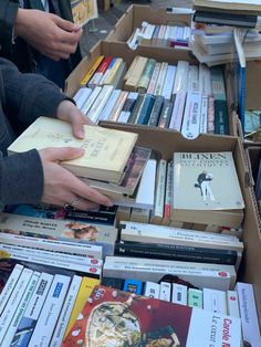 several people are looking at books in a book sale area with boxes full of them