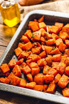 a pan filled with cooked carrots on top of a wooden table next to a bottle of oil