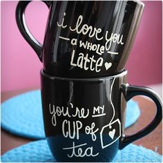 two black coffee mugs sitting on top of a blue place mat next to each other