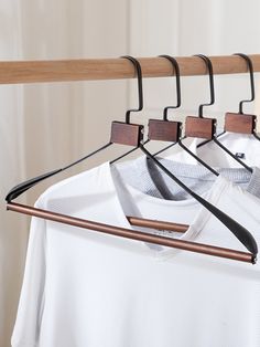 three shirts hanging on clothes hangers in front of a white wall and wooden rail