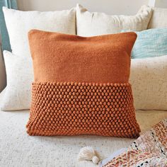 an orange pillow sitting on top of a white bed next to pillows with tassels