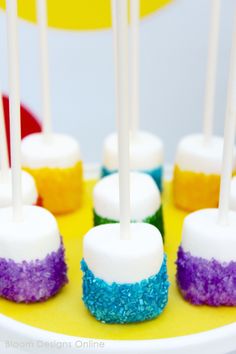 colorful cake pops with white and blue icing on a yellow plate next to candy lollipops