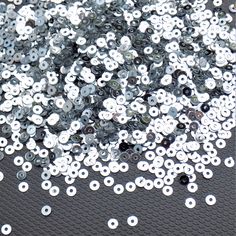 silver and white sequins are scattered on a black surface with holes in the middle