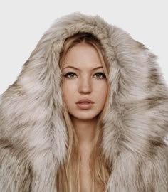 a woman with long hair wearing a fur coat and posing in front of the camera