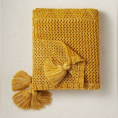 a yellow knitted blanket with tassels and a scarf on the wall next to it