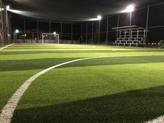 an empty soccer field at night with lights on the goal posts and grass in the foreground