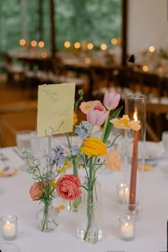 flowers in vases on a table with candles and note pinned to the wall behind them