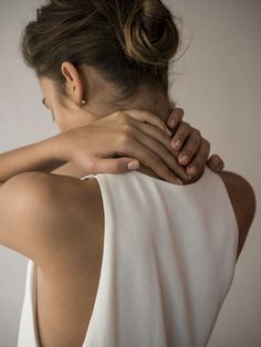 a woman with her back to the camera, holding her hands on her shoulder and looking down