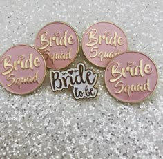 four pink and gold bride to be badges sitting on top of a glittery surface