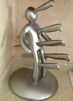 a metal sculpture of a person holding several knives in his hand, on top of a counter