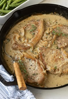 some meat and gravy in a skillet with green beans on the side