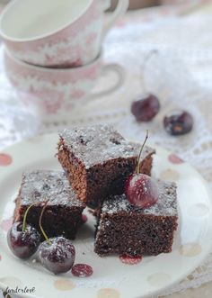 two pieces of chocolate cake with cherries on a plate next to a cup and saucer