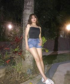 a young woman standing next to a tree in front of a street light at night