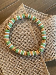 a bracelet with green, yellow and white beads on a piece of burlock