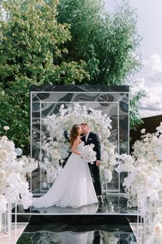 a bride and groom are kissing in front of an arrangement of white flowers at their wedding