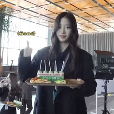 a woman holding a tray with cake on it and pointing at the camera while another person stands behind her