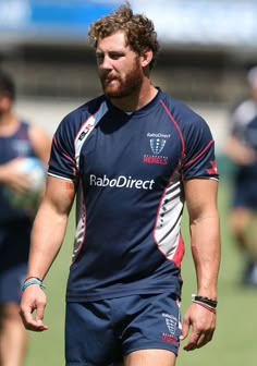 a man with a beard is walking on the field wearing shorts and holding a frisbee