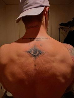 the back of a man with tattoos on his upper and lower back, wearing a baseball cap