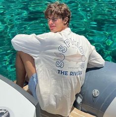 a young man sitting on top of a boat in the water