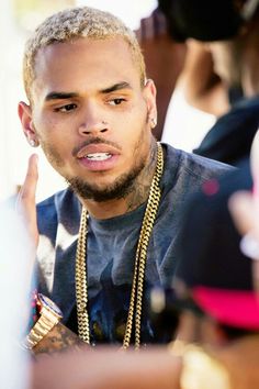 a close up of a person wearing a necklace and holding a cell phone to his ear