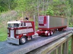 a toy semi truck is parked on the side of a rail road bridge in front of some trees