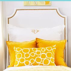 a bed with yellow and white pillows on top of it next to a painting above the headboard