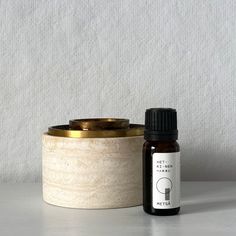 a bottle of essential oil next to a container with an empty lid on a white surface