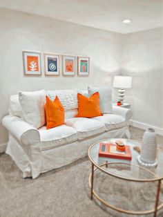 a living room with white couches and orange pillows