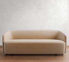 a beige couch sitting on top of a wooden floor next to a white wall in an empty room