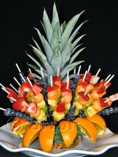 an arrangement of fruit is arranged on a white platter with pineapples, oranges and strawberries