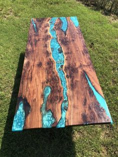 a long wooden table with blue paint on it in the grass next to some trees