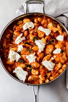 a pan filled with pasta and cheese on top of a white tablecloth next to a spoon