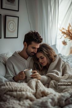 a man and woman cuddle in bed while looking at their cell phone, holding a cup