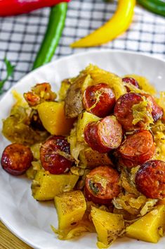 a white plate topped with sausages and potatoes next to peppers on a wooden table