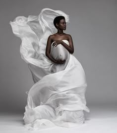 a woman in a white dress is posing with her arms wrapped around her body and flowing fabric