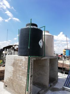 two large tanks sitting next to each other on top of a cement block with green piping