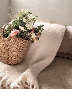 a basket filled with flowers sitting on top of a bed next to a white blanket