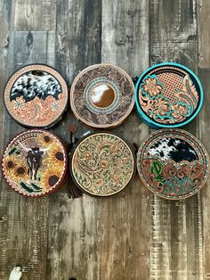 four plates with designs on them sitting on a wooden surface