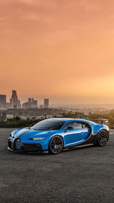 a blue bugatti is parked in front of a cityscape at sunset