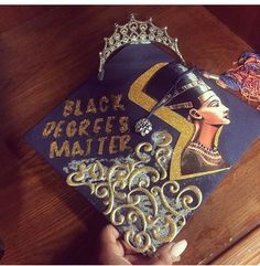 a black queen's matter graduation cap is being held by a person wearing a tiara