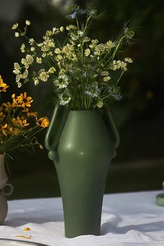 two vases with flowers in them sitting on a white table cloth next to each other