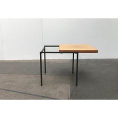 a wooden table sitting on top of a cement floor next to a white wall in an empty room