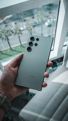 a person holding up a silver cell phone in front of a window with palm trees