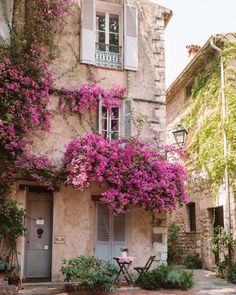 an old building with pink flowers on the windows and shutters in front of it