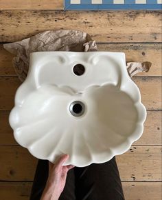 a person holding a white ceramic sink in front of a wooden wall with paper on it