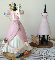 there are two figurines on the table next to each other, one is wearing a pink dress